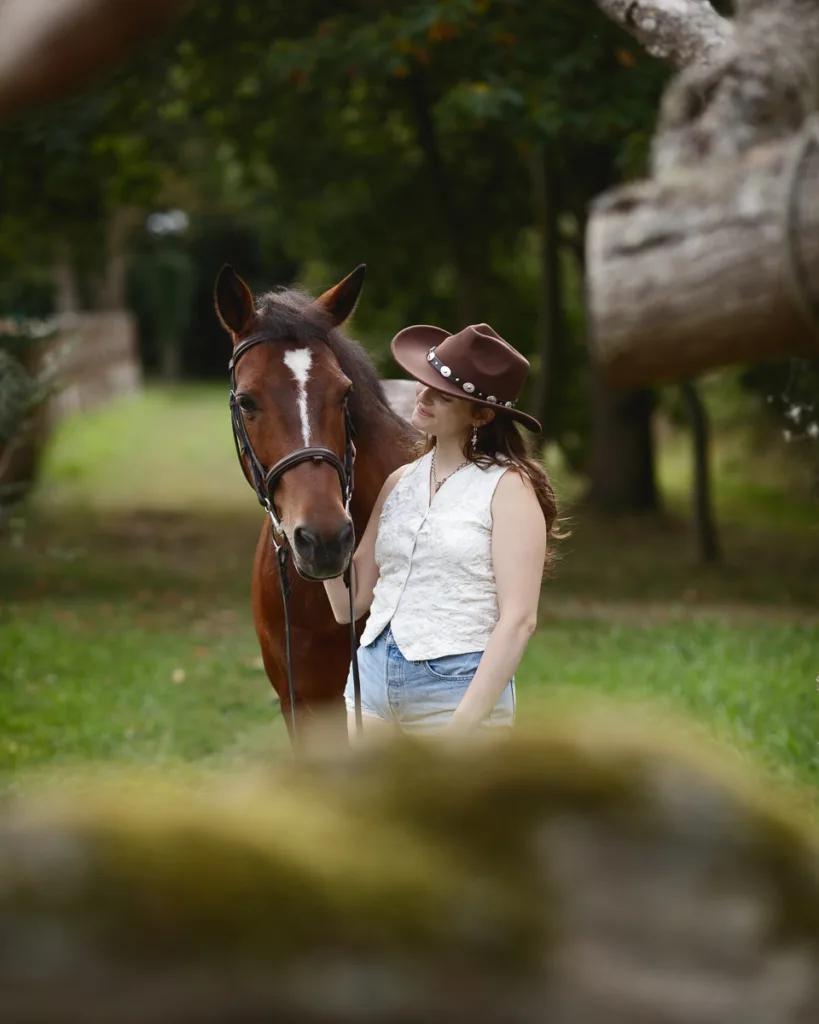 Woman in hat with brown horse, outdoor setting.