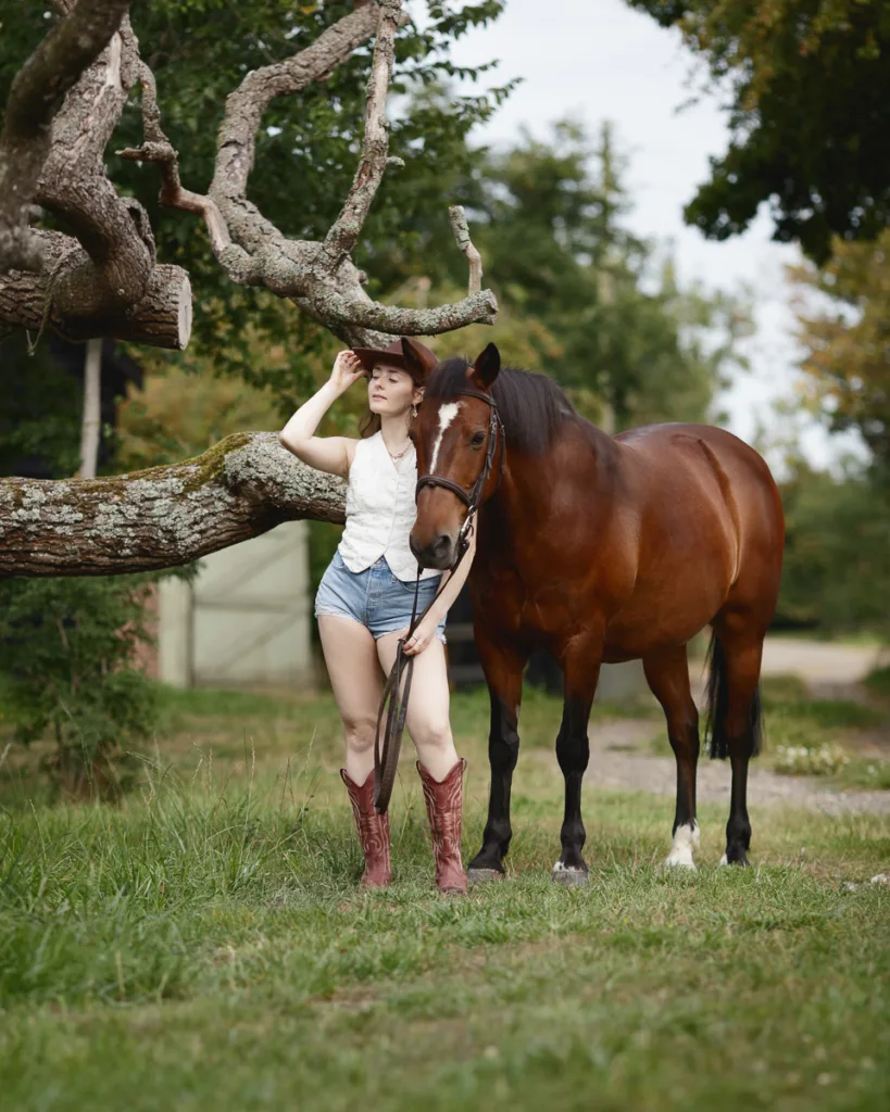 Woman in cowboy hat with horse under tree.