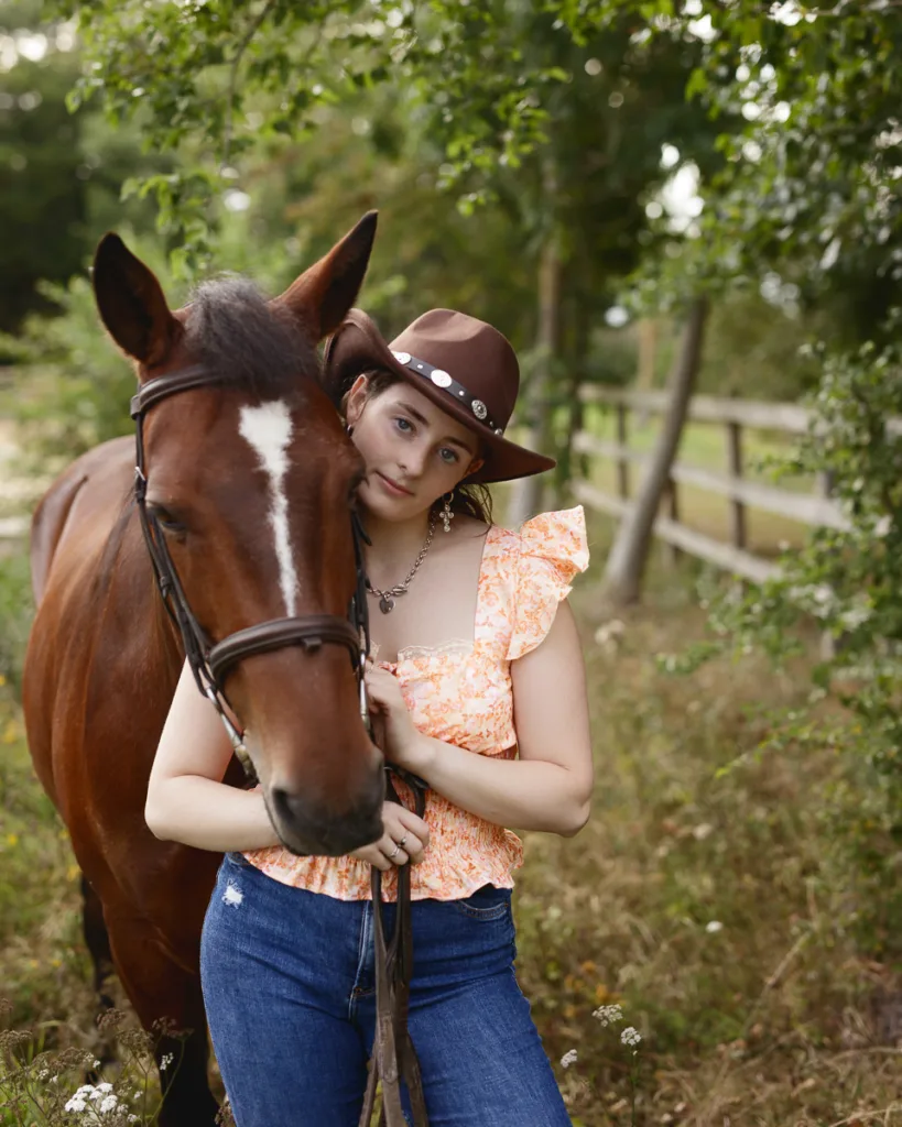 Woman in hat with brown horse outdoors.
