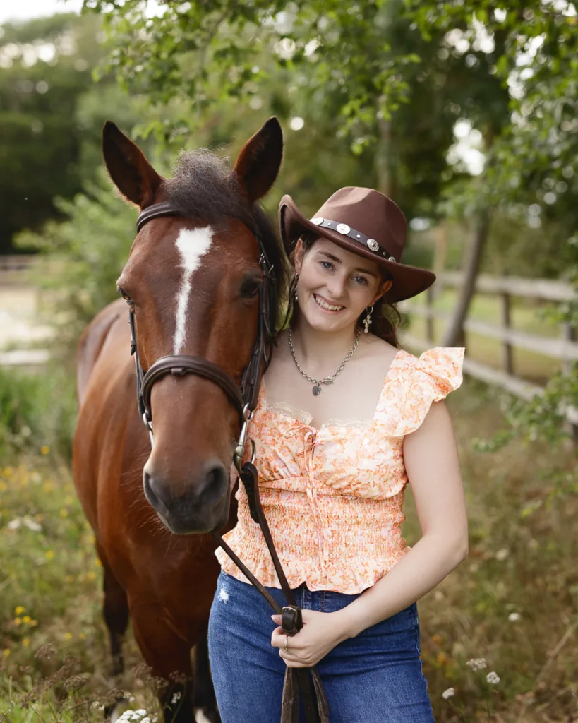 Smiling woman in cowboy hat with brown horse outdoors.