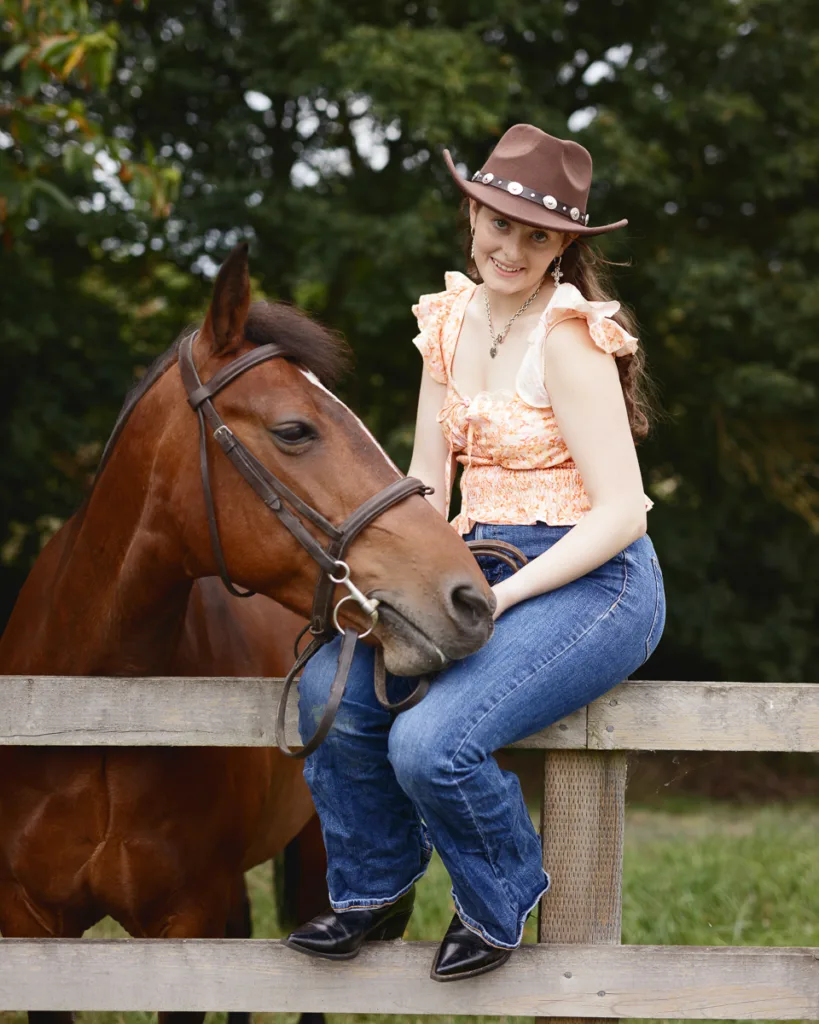 Woman in cowgirl hat with horse on fence.