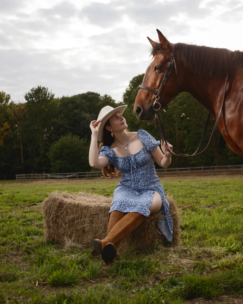 Woman sitting on hay bale with horse.
