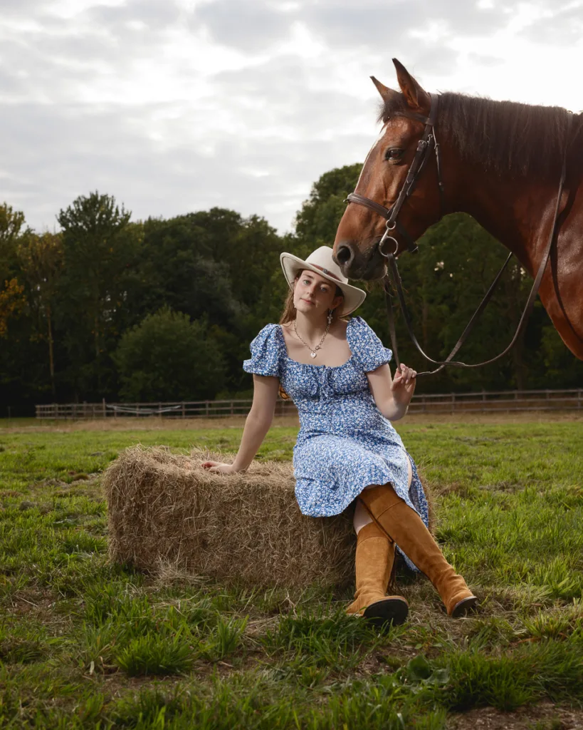 Woman in countryside with horse and hay bale.