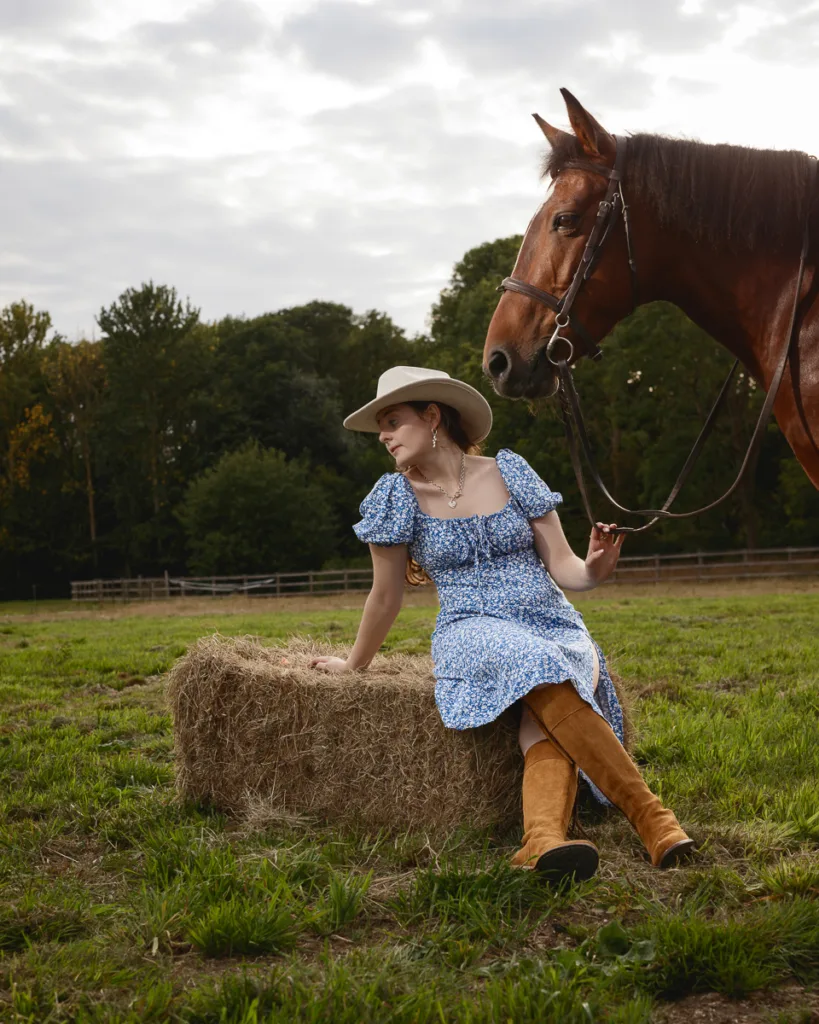 Woman with horse sitting on hay bale outdoors.