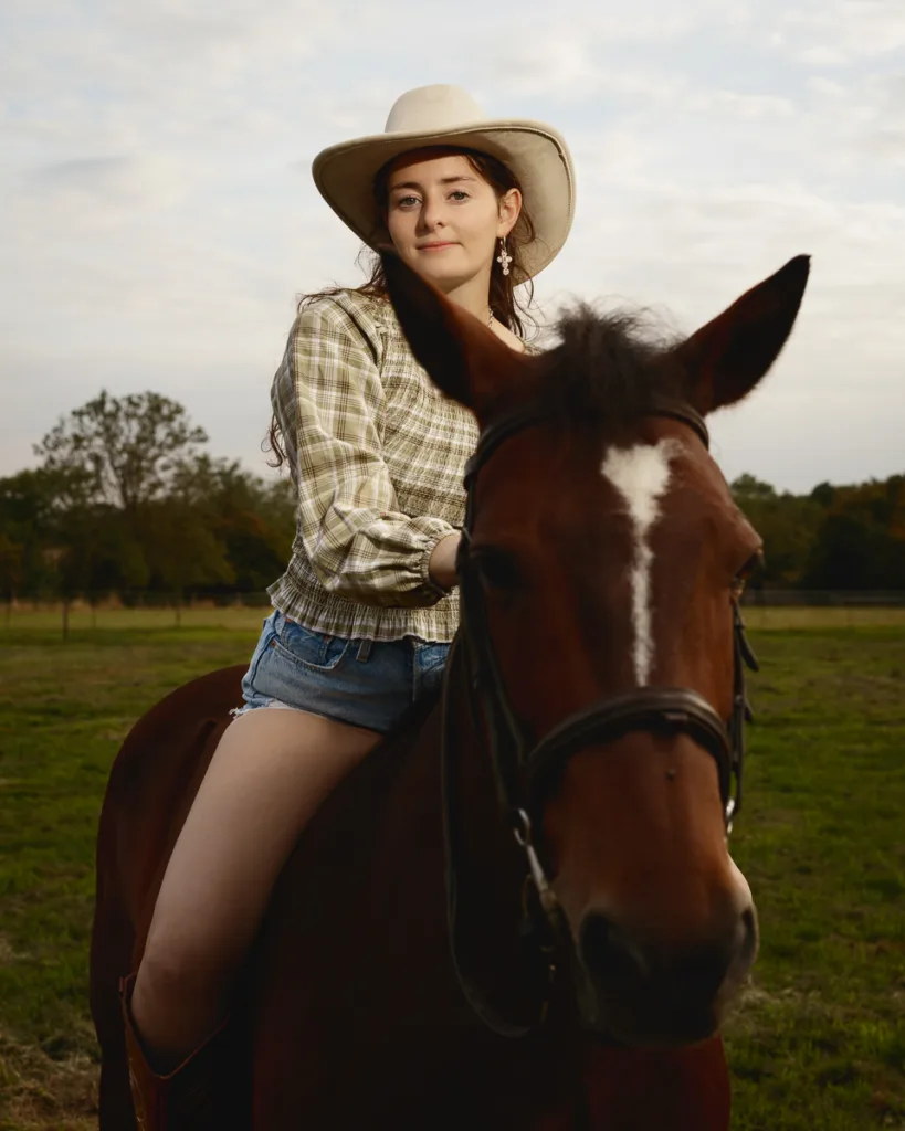 Cowgirl riding horse in countryside setting.
