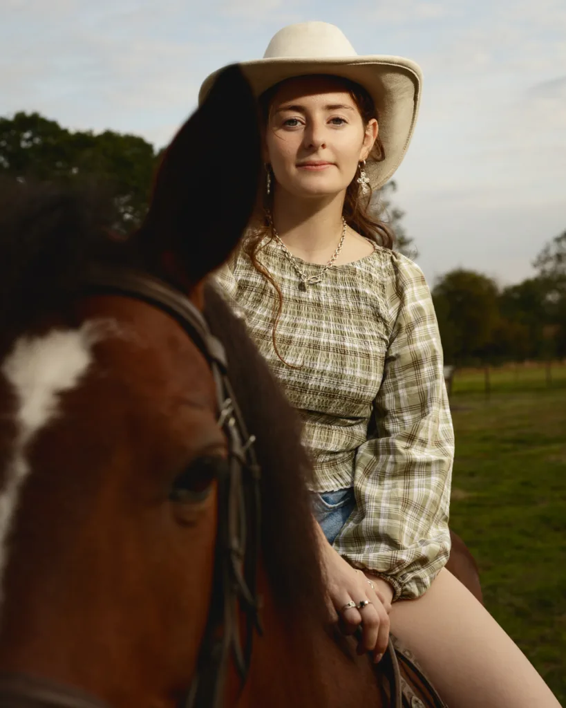 Woman in cowboy hat riding a horse outdoors.