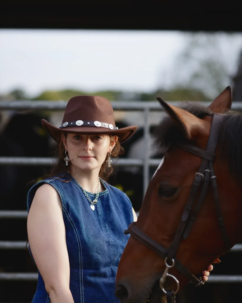 Person wearing cowboy hat with horse nearby.