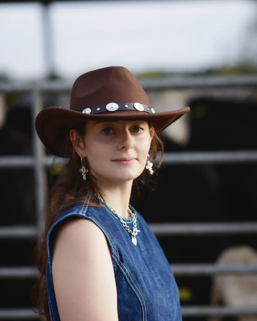 Woman in cowboy hat and denim dress outdoors.