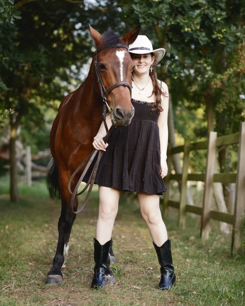 Woman in dress and hat with horse outdoors.
