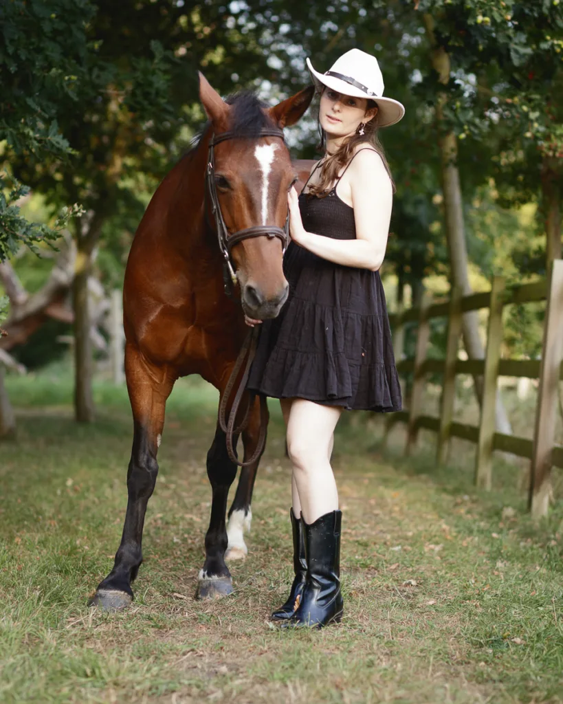 Woman in hat with horse on countryside path.