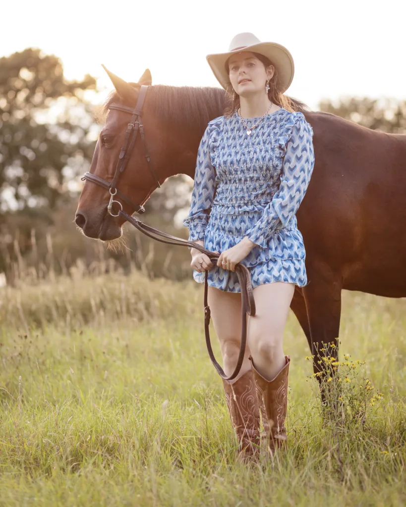 Woman in cowboy attire with horse in field