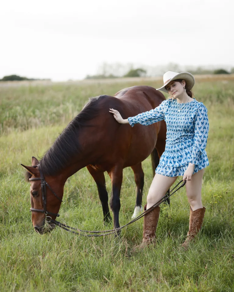 Woman in field with horse, wearing cowboy hat.