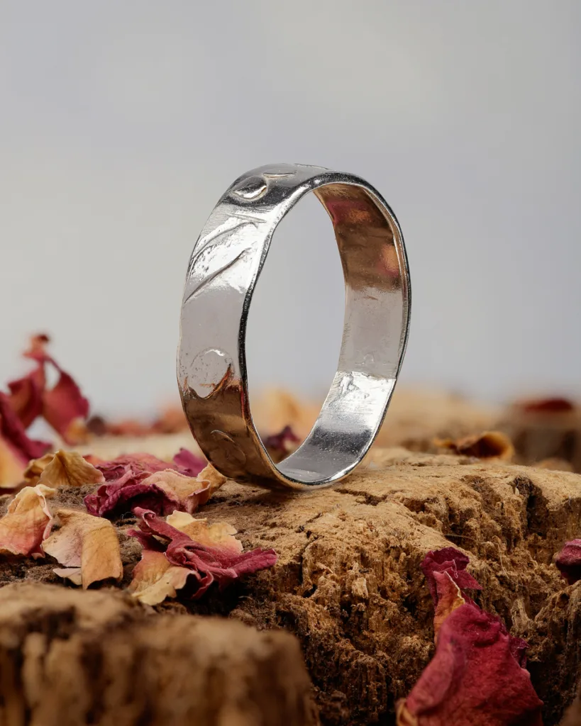 Silver ring on bark with dried petals.