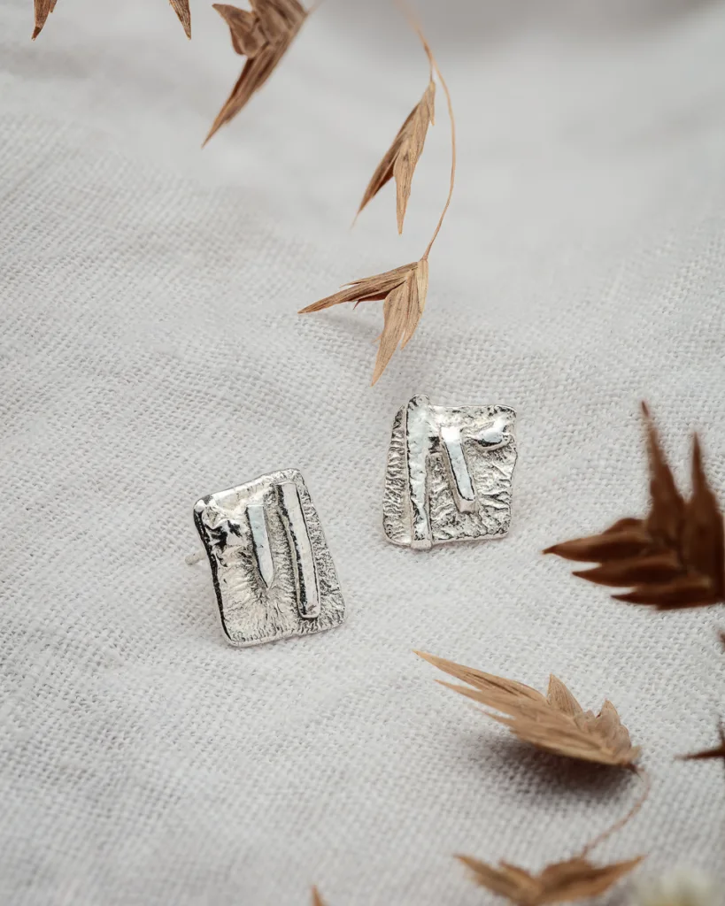 Silver textured earrings on fabric background.