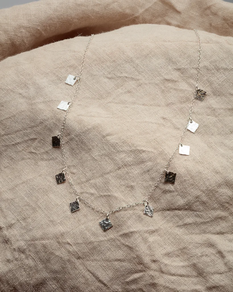 Silver charm necklace on beige fabric.