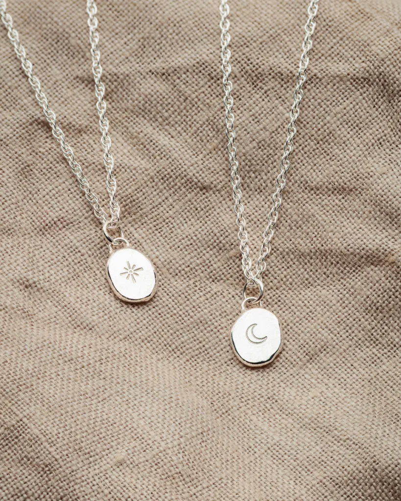 Silver sun and moon pendant necklaces on fabric.