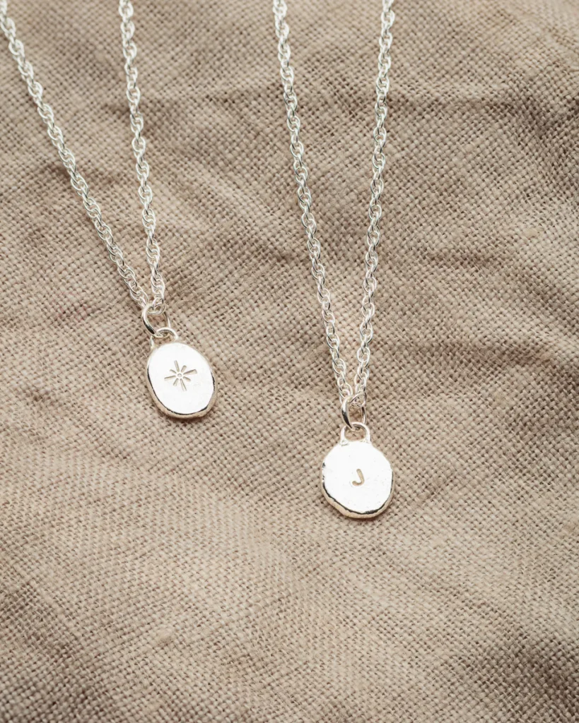 Silver pendant necklaces on textured fabric background.