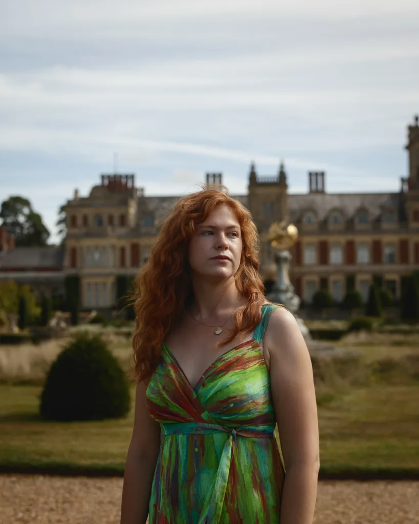 Woman in colourful dress outside a stately home.