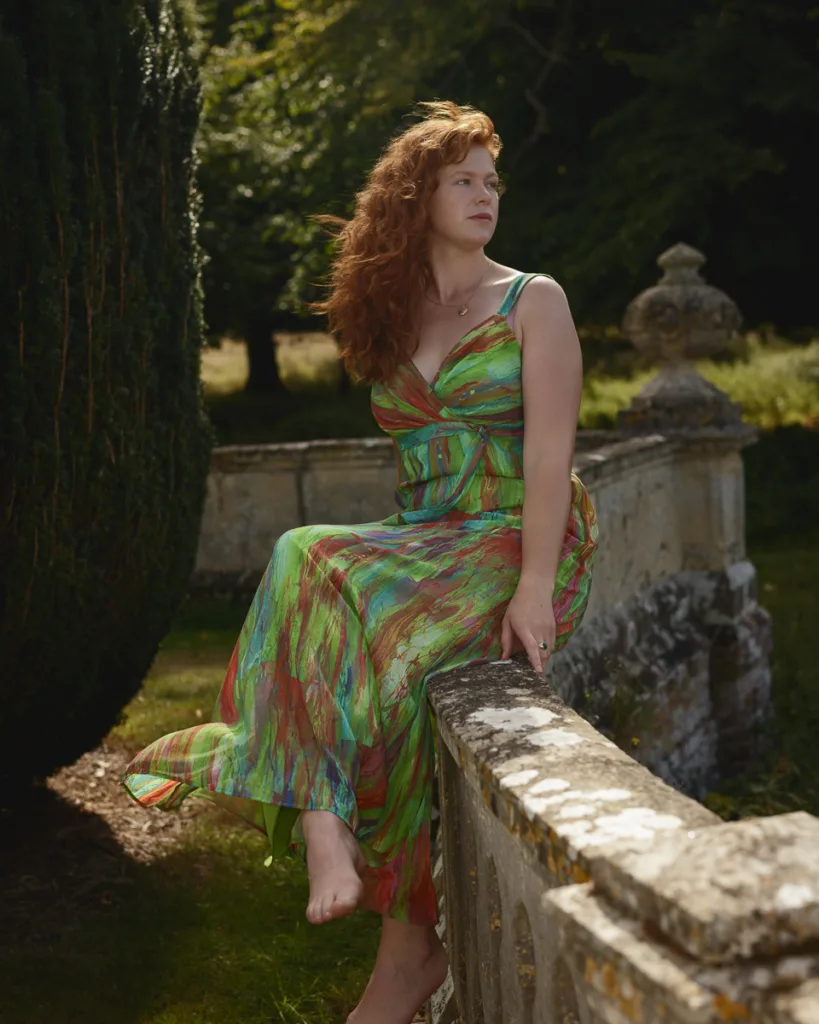 Woman in colourful dress sitting on stone railing outdoors.