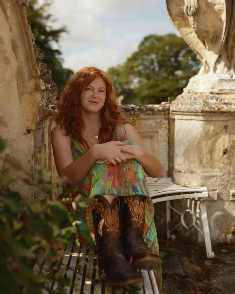 Woman in colourful dress and boots on bench outdoors.