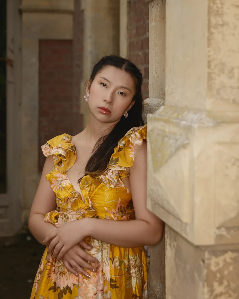 Person in floral dress leaning against stone wall.