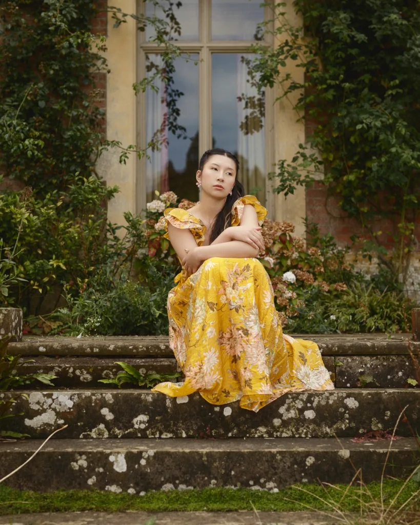 Woman in yellow dress sitting on garden steps.