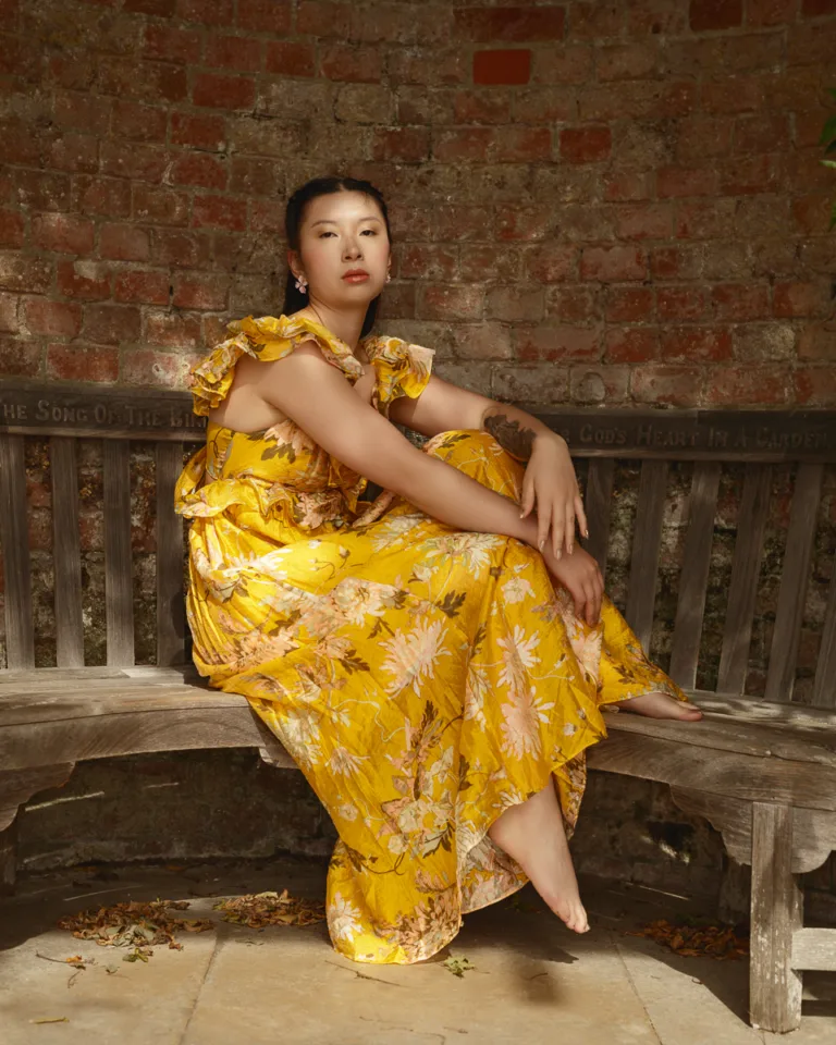 Woman in yellow floral dress sitting on bench.