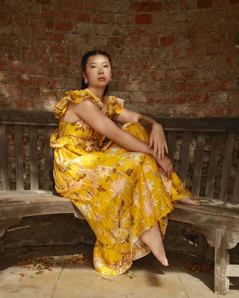 Woman in yellow floral dress sitting on bench.