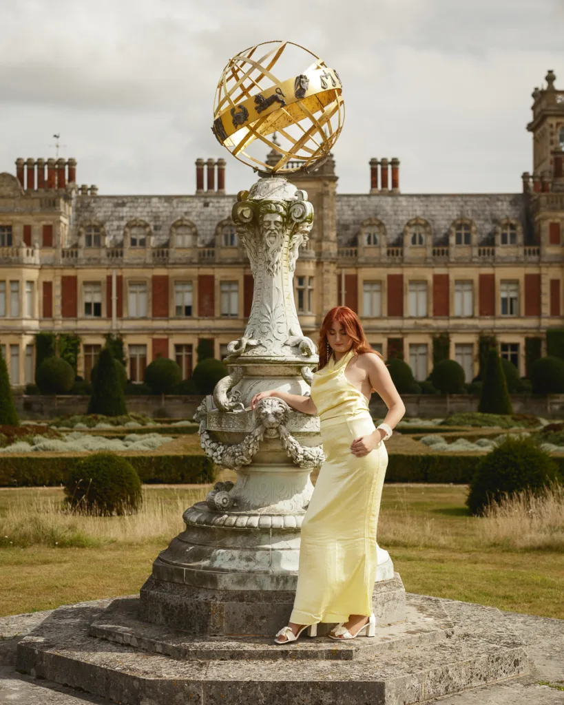 Woman in yellow dress beside ornate garden sundial.