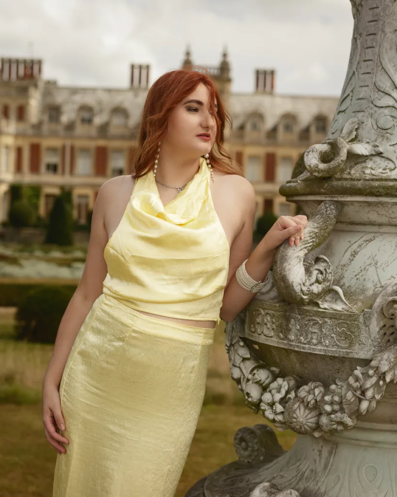 Woman in yellow dress near ornate statue outdoors.