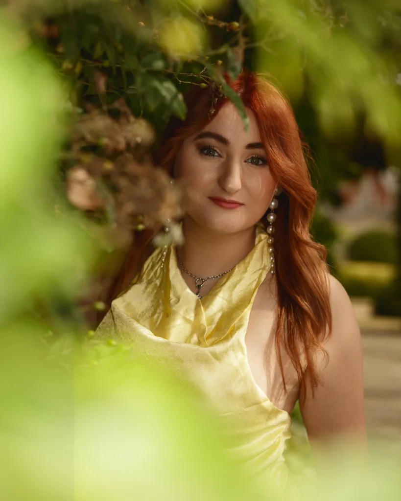 Woman in yellow dress among green leaves.