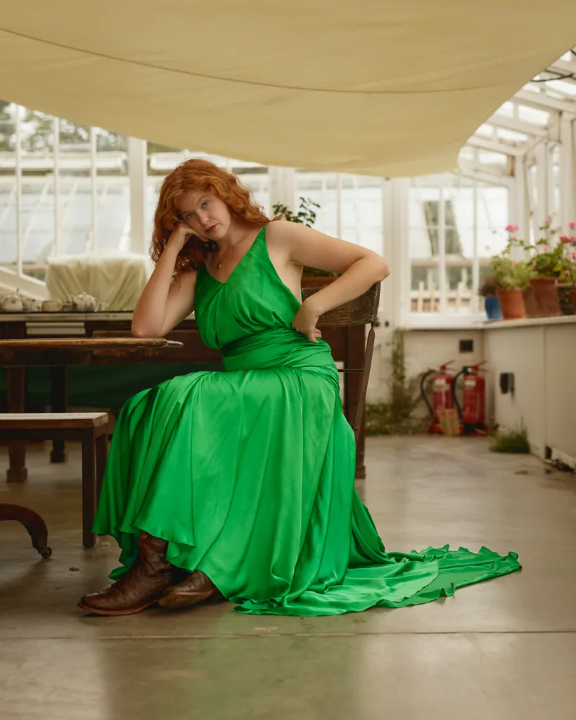 Woman in green dress sitting in a conservatory.