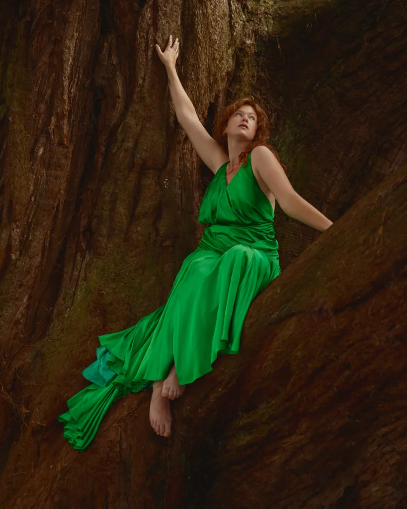 Woman in green dress sitting on tree trunk.