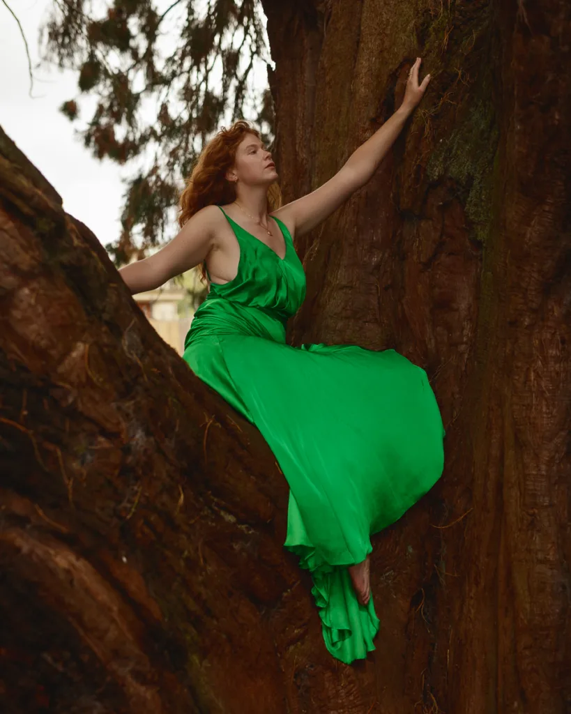 Woman in green dress sitting on tree trunk.