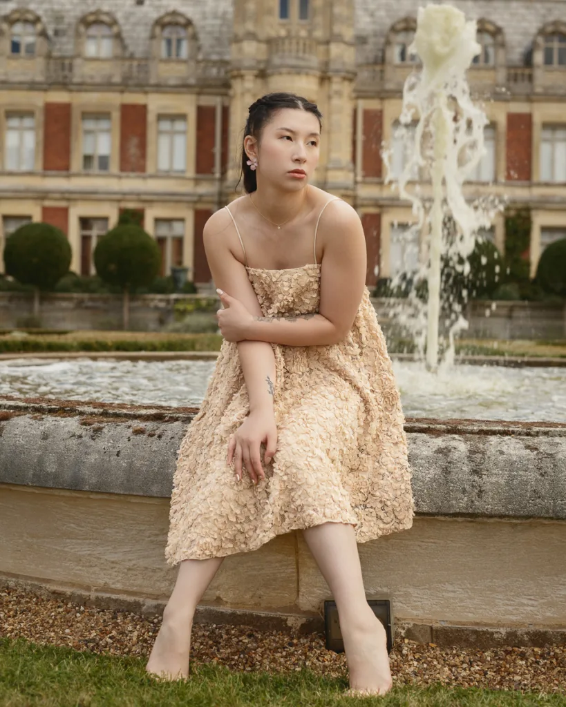Person in beige dress by fountain, elegant scenery.
