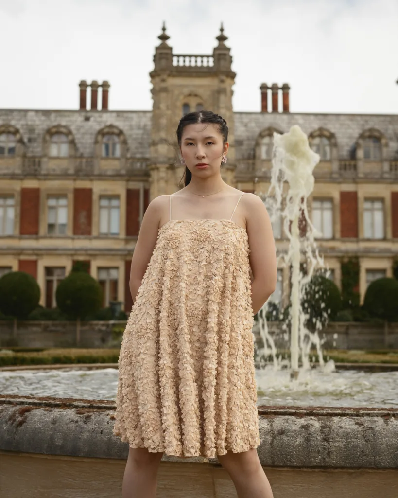 Woman in textured dress by historic building fountain.