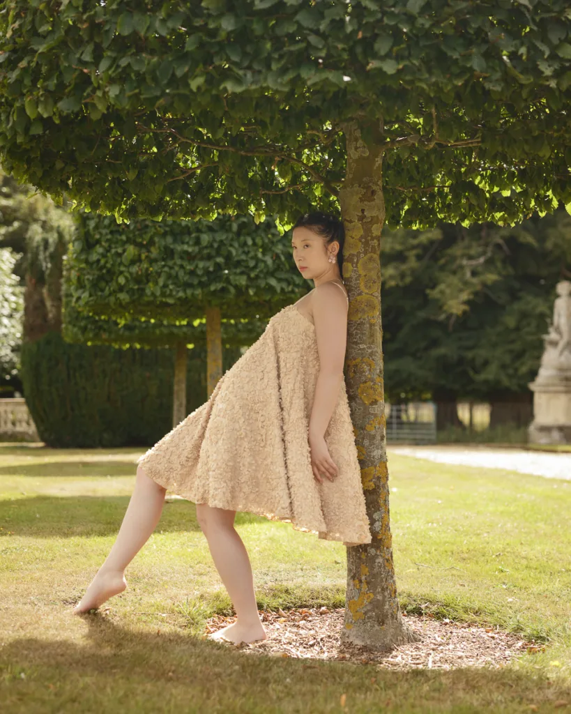 Woman in a floral dress leaning against a tree.
