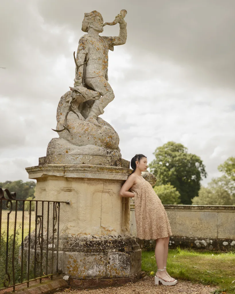 Woman in beige dress near historic statue outdoors.