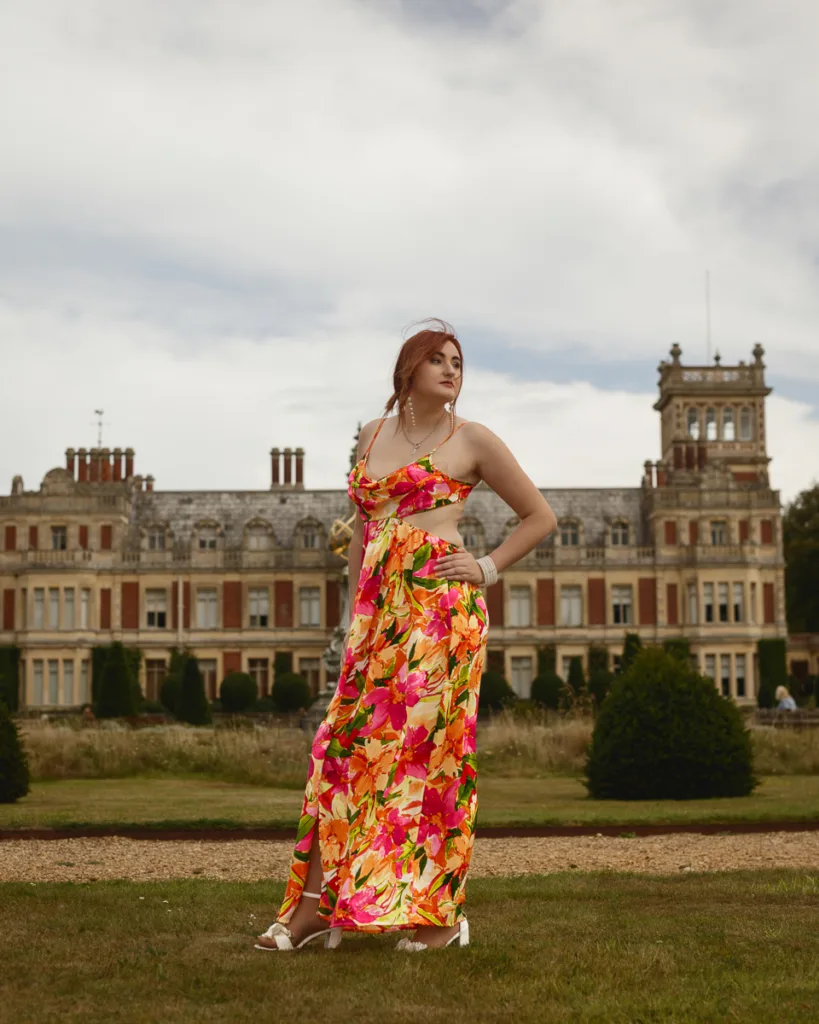 Woman in floral dress in front of mansion.