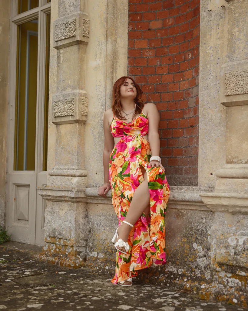 Person in floral dress leaning against brick wall