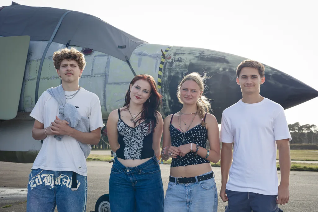 Young adults standing by an old aircraft outside.