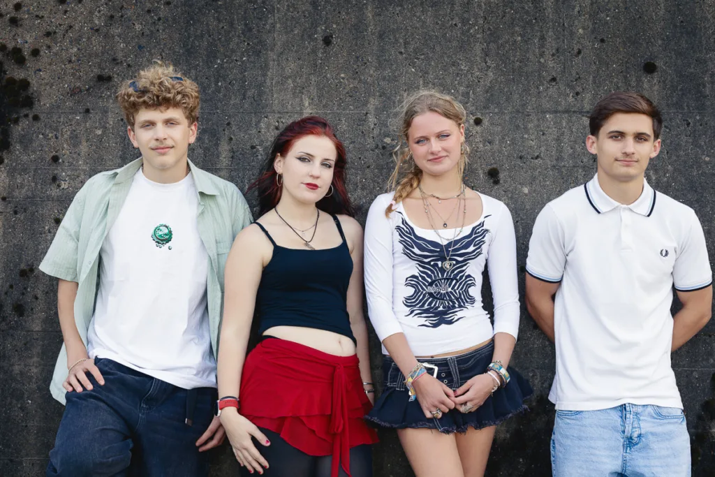 Four teenagers stand against a concrete wall.