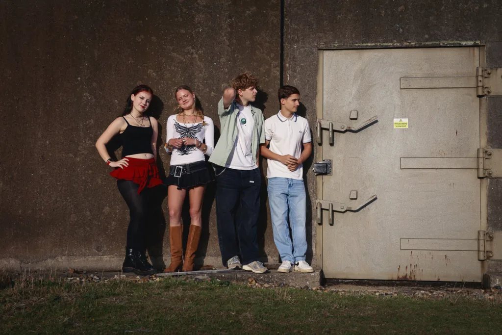 Four people standing by a concrete wall and door.