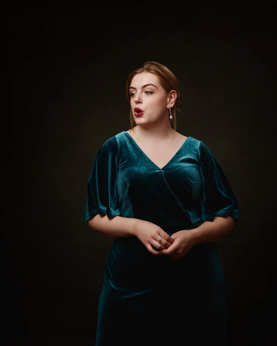 Woman in teal dress singing on dark background.