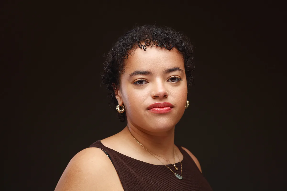 Person posing with curly hair and earrings.