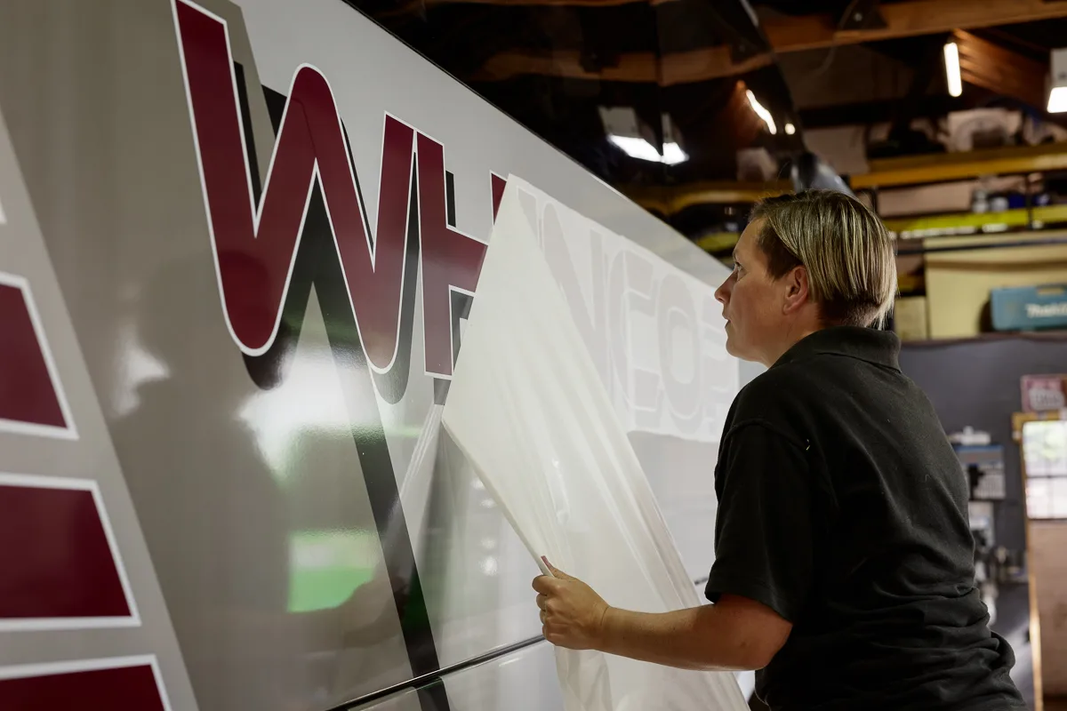 Person applying a large decal onto bus side.