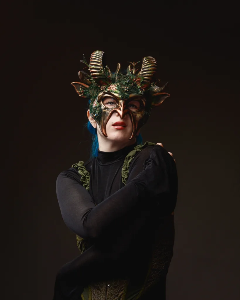 Person in intricate horned mask, dark background.
