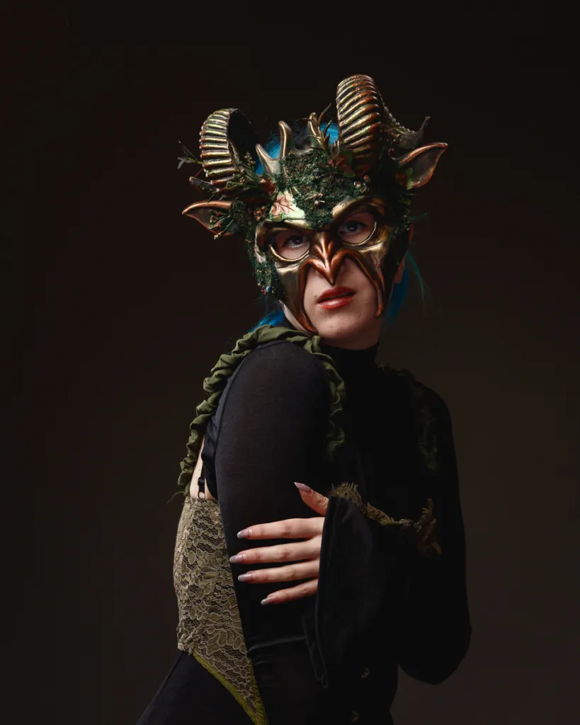Person wearing ornate fantasy horned mask, dark attire
