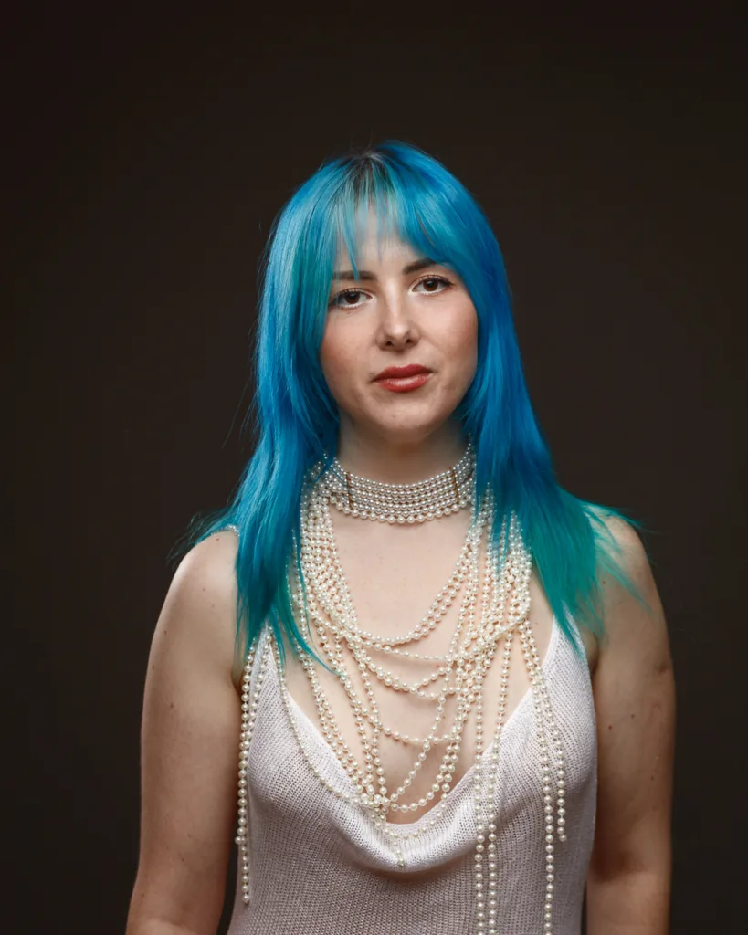Person with blue hair, wearing pearl necklaces.
