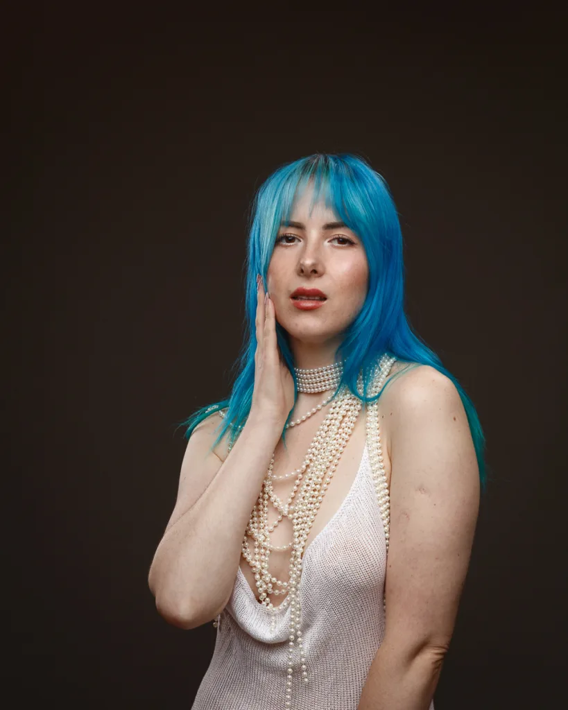 Woman with blue hair and pearl necklaces.